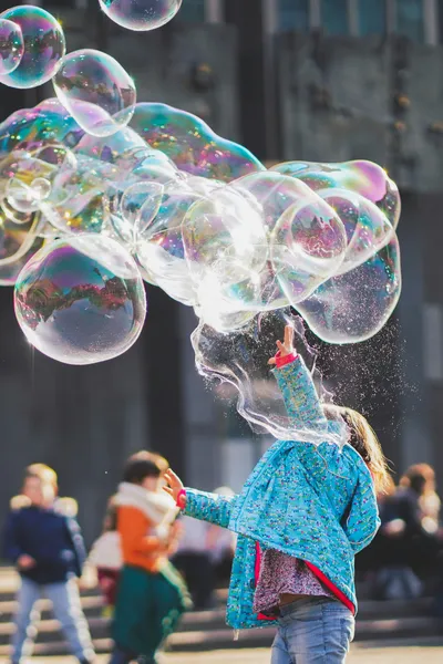 Child reaching for large iridescent soap bubbles in sunlight